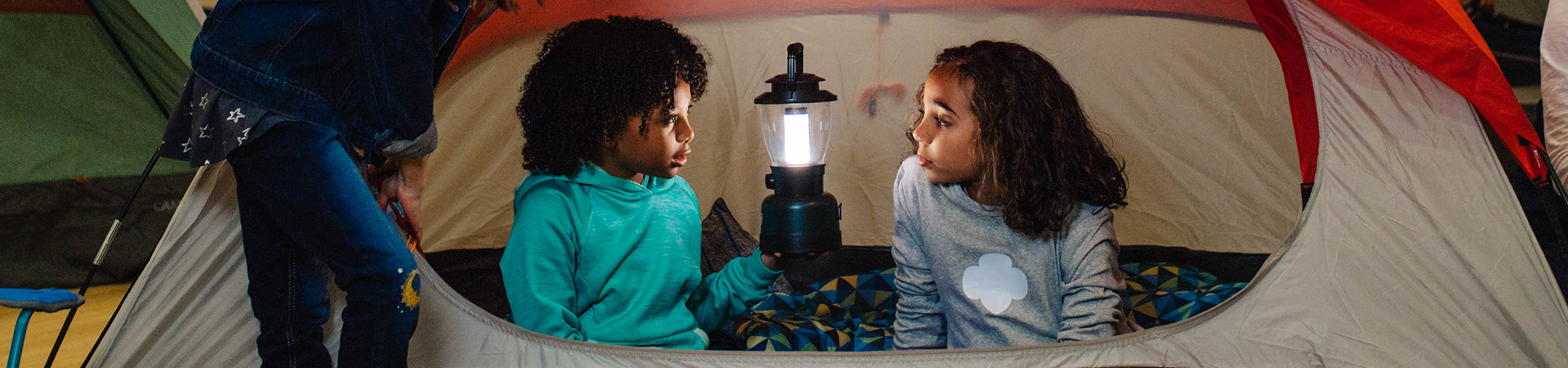  two girls in a tent talking by lantern light 