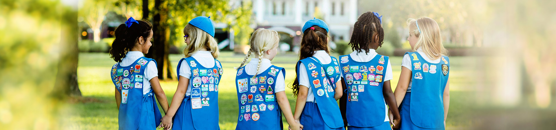  Daisy Girl Scouts holding hands and showing off their uniforms filled with patches 