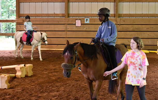 riding instructor-in-training leading young rider on a brown horse around arena