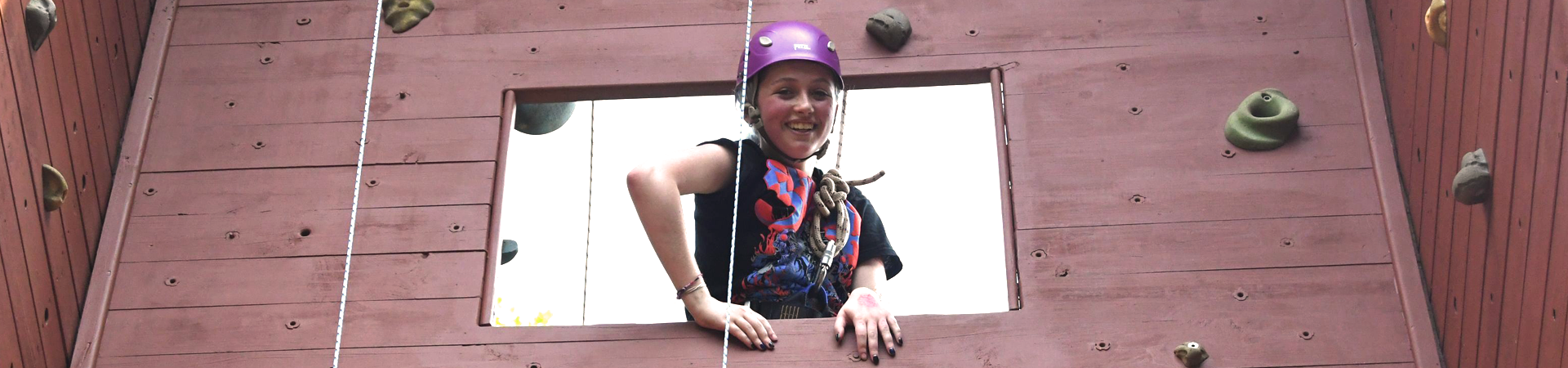  girl smiling on climbing rock wall with helmet on 