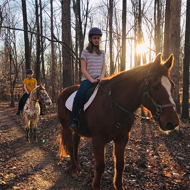 two girls riding horses on a trail in the woods