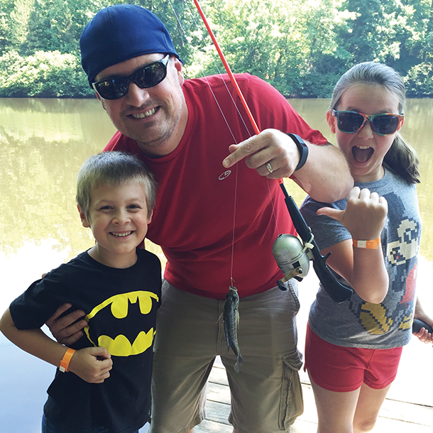 little boy showing off the fish he caught with his dad and sister cheering for him