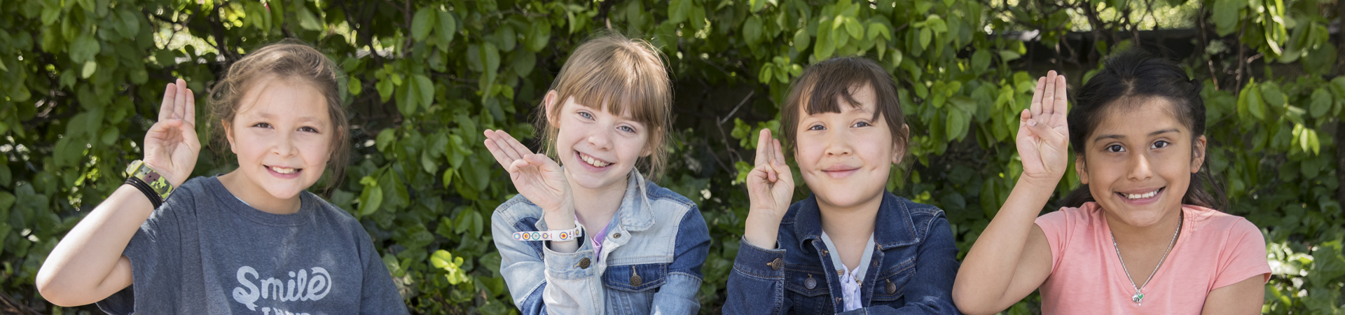  four girls smiling showing the Girl Scout hand sign 