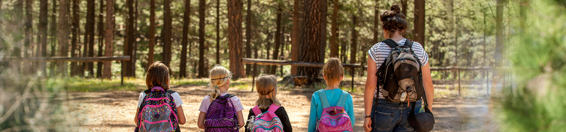  group of girls with backpacks walking through wood with adult volunteer 